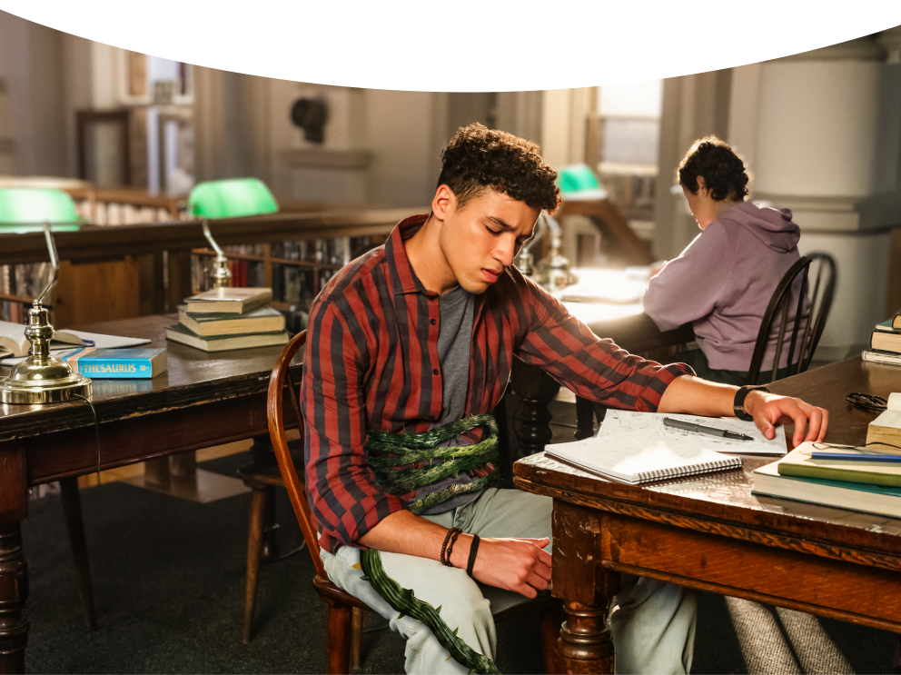 Adult male student sitting in discomfort at the library with a green vine wrapped around his stomach