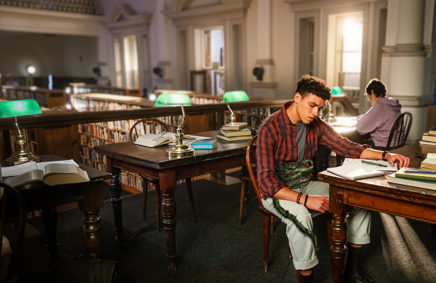 Adult male student sitting in discomfort at the library with a green vine wrapped around his stomach
