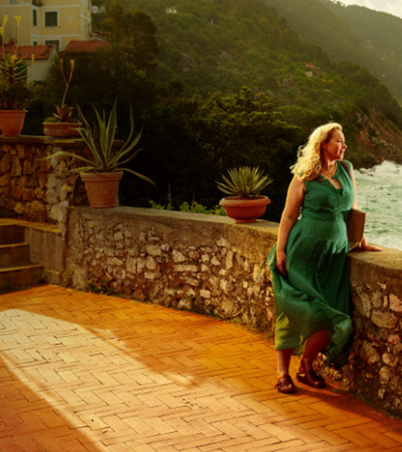 Woman in a green dress leaning on a stone wall overlooking the coast