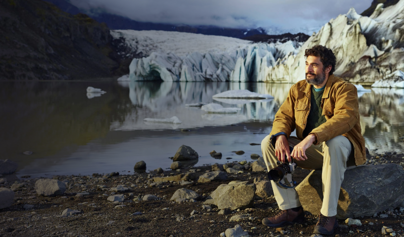 Man sitting on a rock looking out into the distance with water and mountains behind him