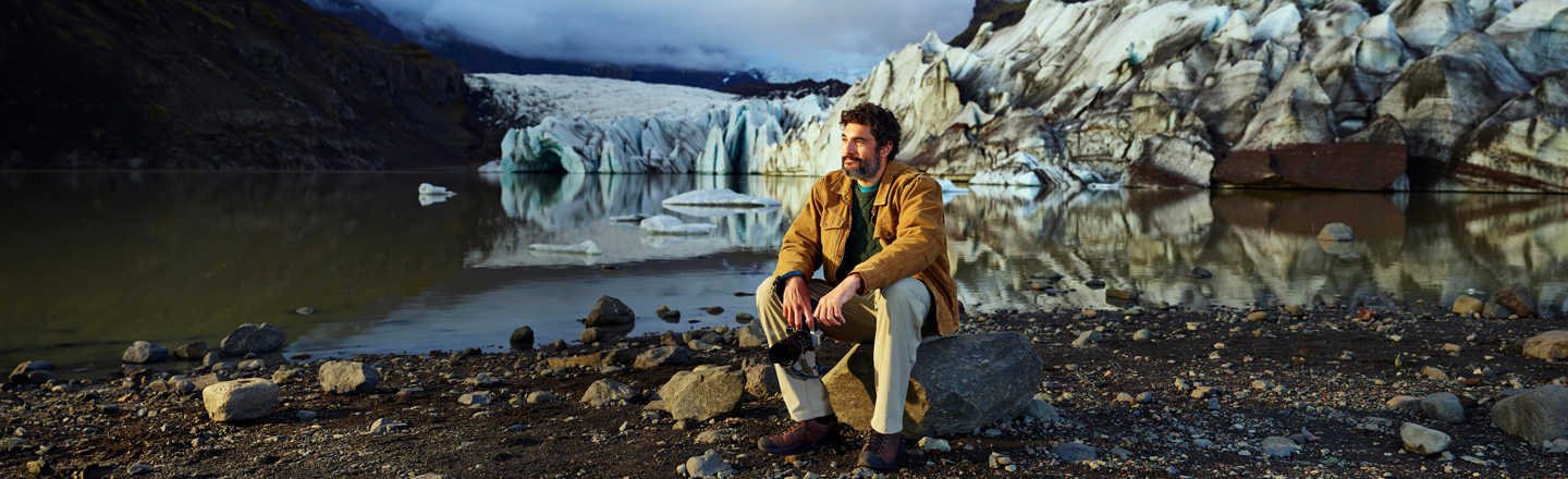 Man sitting on a rock looking out into the distance with water and mountains behind him