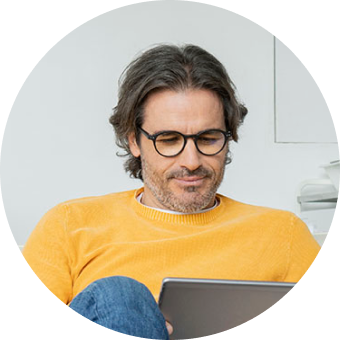 Man in orange shirt and wearing glasses looking down at laptop