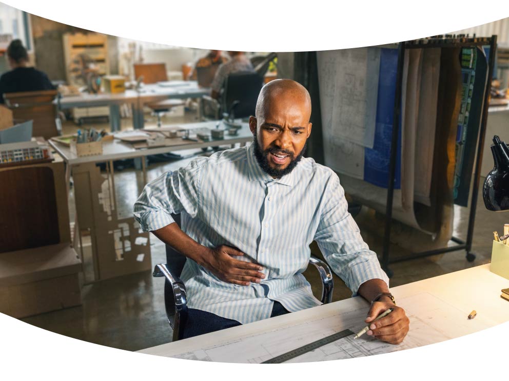 Man sitting at desk holding his stomach in discomfort
